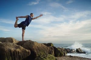 Man doing yoga on rocks with waves crashing in Bournemouth