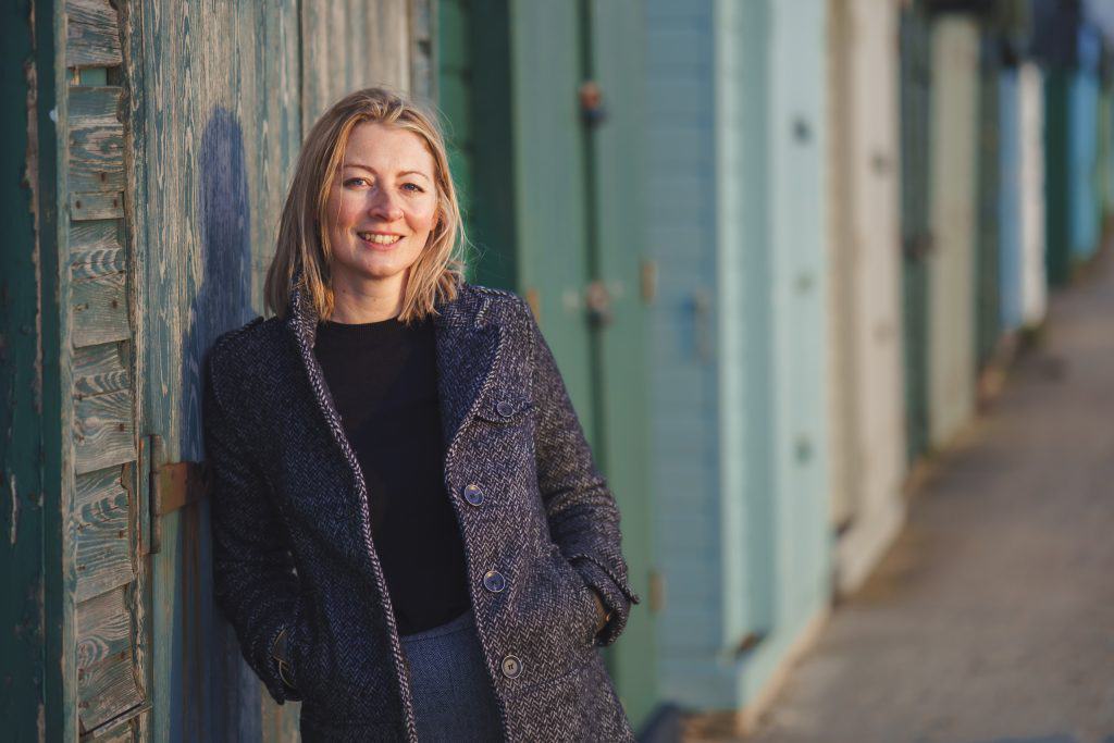 Relaxed portrait of a woman standing by a weathered beach hut in winter, natural light, Bournemouth coast